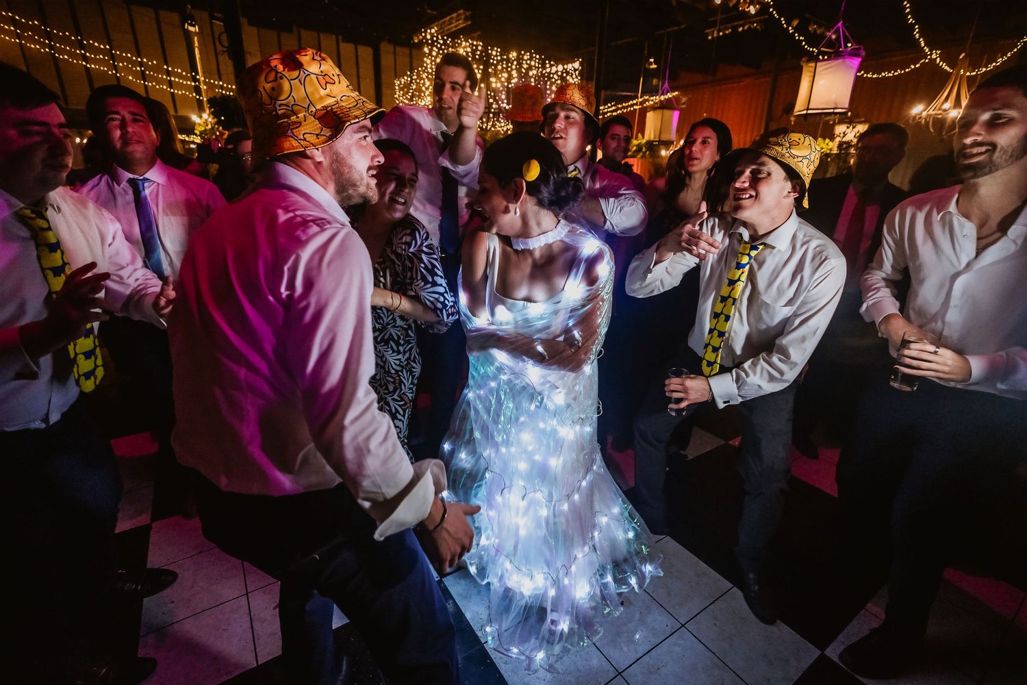 Bride in light-up wedding dress dancing with groom surrounded by guests at a festive wedding reception.