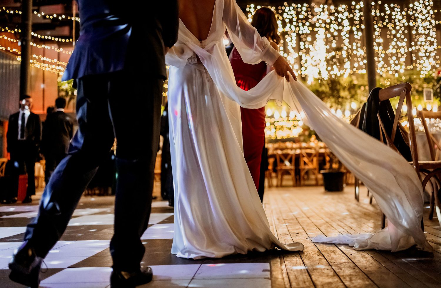 Couple shares first dance in wedding attire under warm string lights at elegant reception venue.