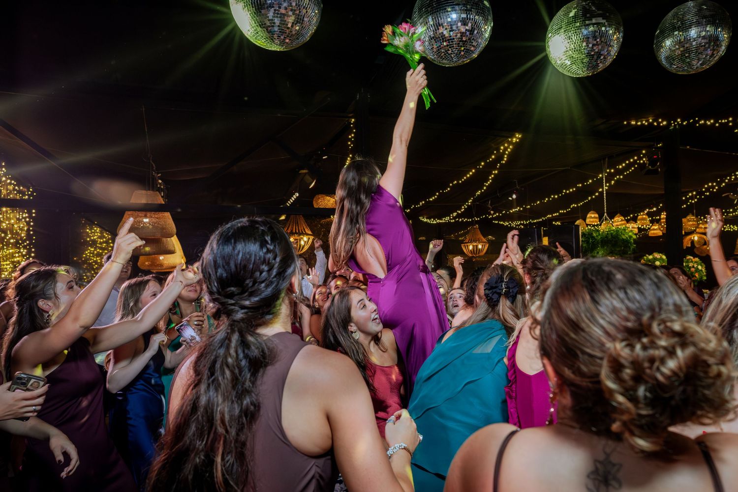 Guest in purple dress catches bridal bouquet triumphantly at wedding reception.