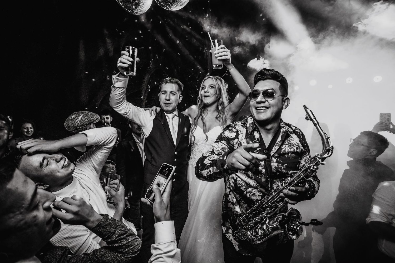Bride and groom toast champagne with saxophonist under disco balls at wedding.