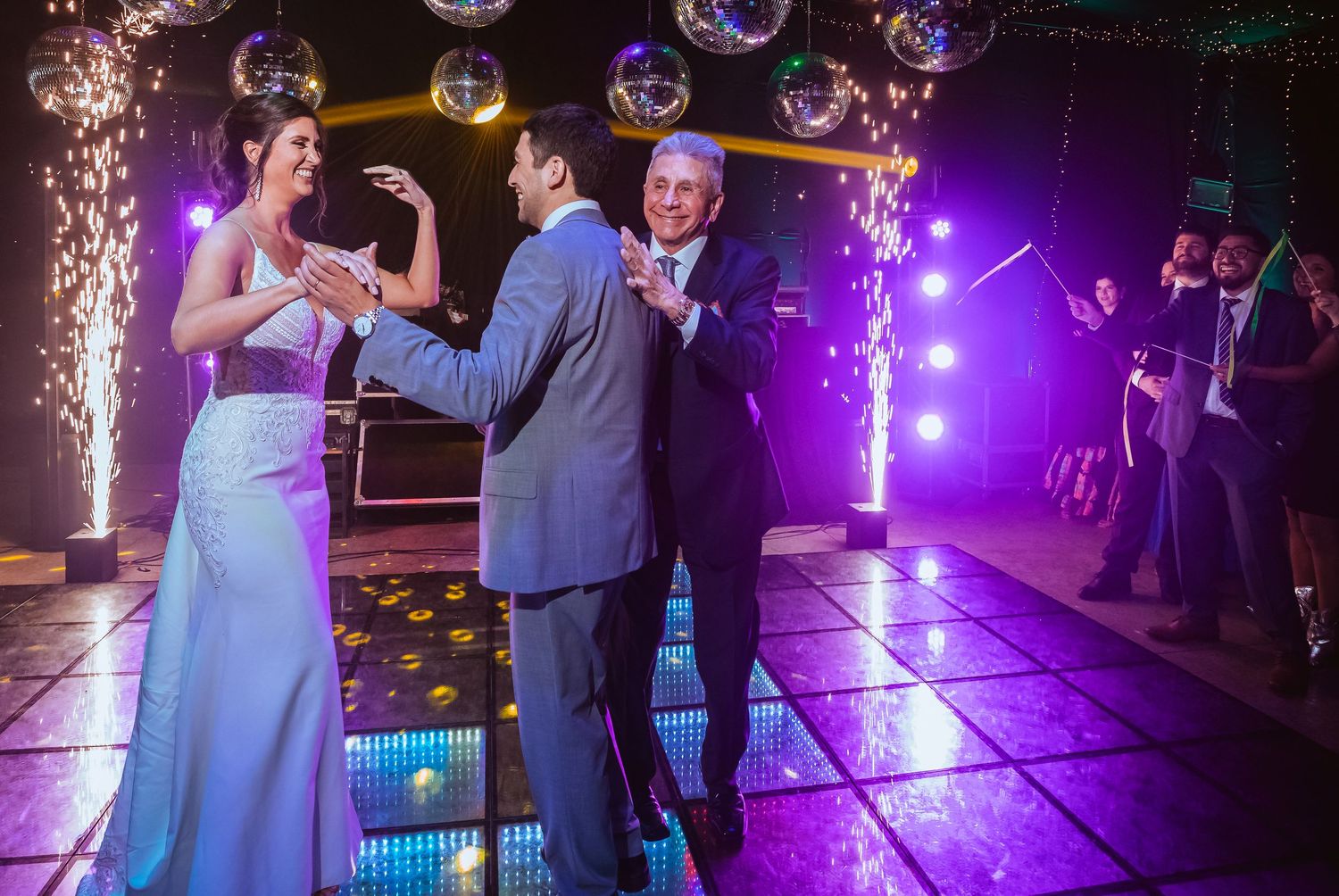 Bride and groom share a joyful first dance with sparklers and disco balls at elegant wedding reception.