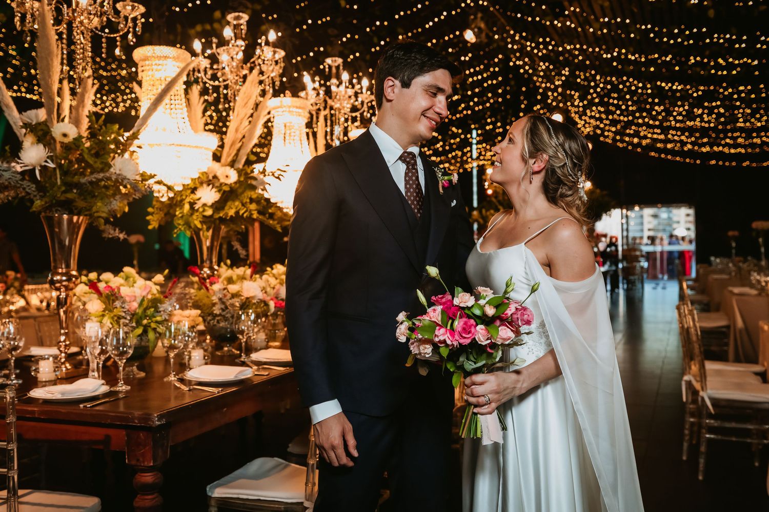 Bride and groom share romantic moment surrounded by fairy lights at wedding reception.