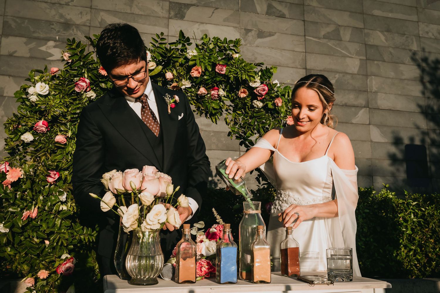 Bride and groom performing a sand unity ceremony at floral-decorated altar.