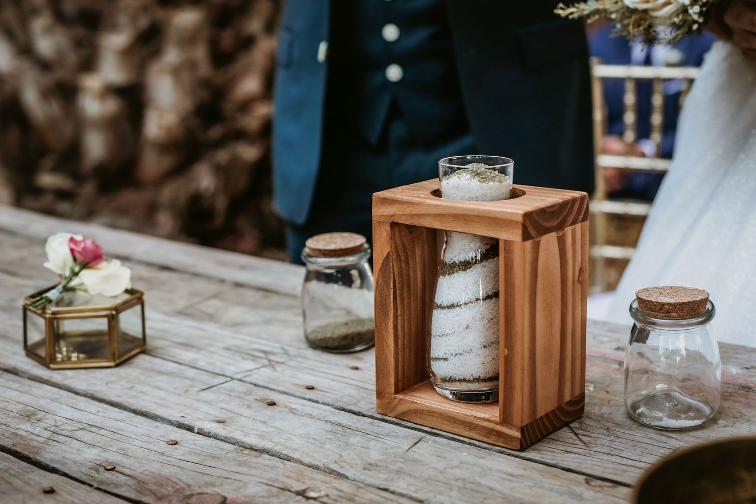 Rustic wooden lantern centerpiece with sand ceremony jars on a weathered wooden table at a wedding.