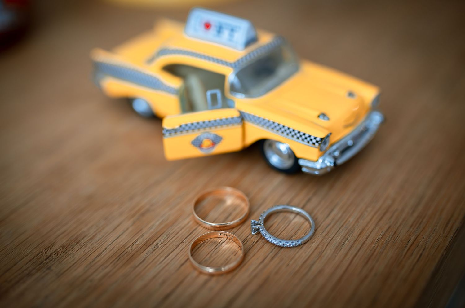 Two gold wedding rings and one diamond ring displayed in front of a yellow toy taxi cab.