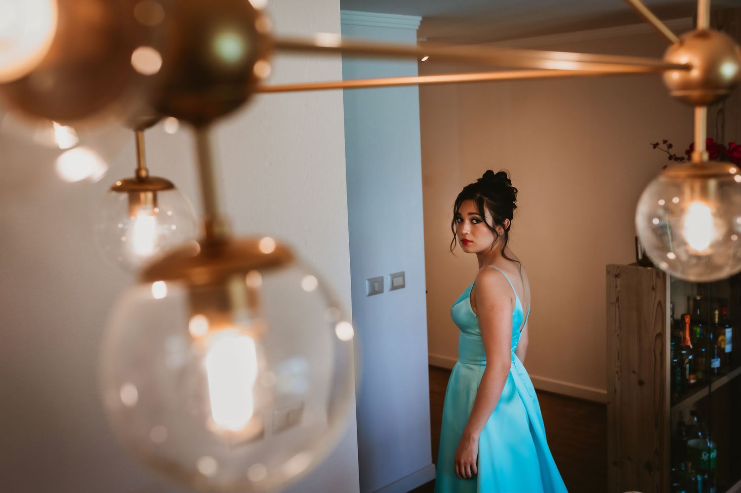 Bride in turquoise gown standing in softly lit room with vintage globe pendant lights.