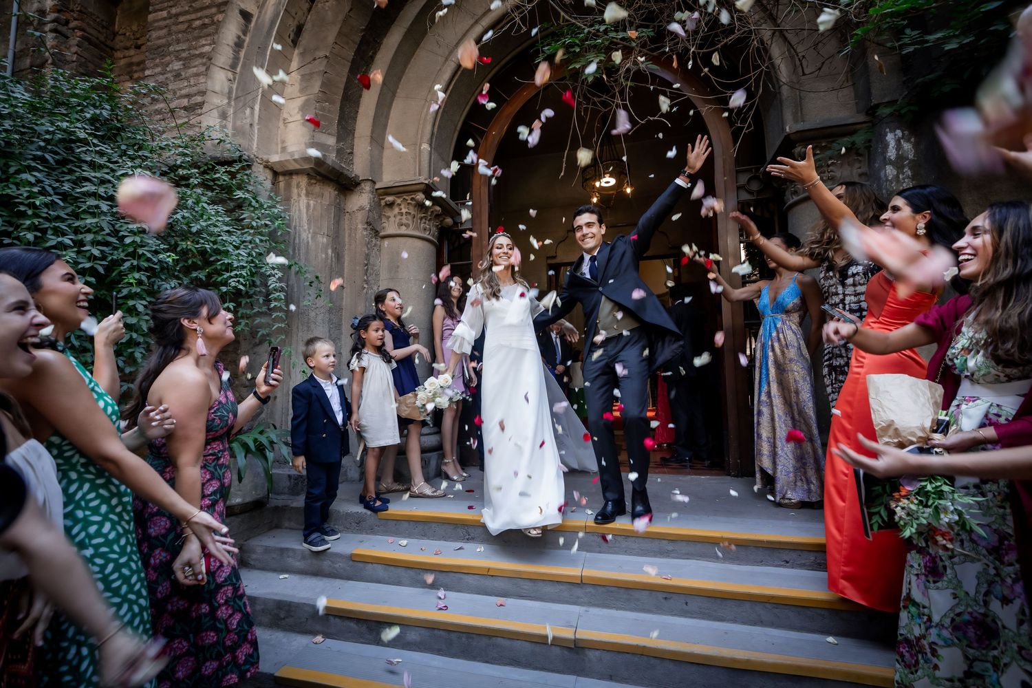 Bride and groom exit church as guests toss flower petals in joyful celebration.