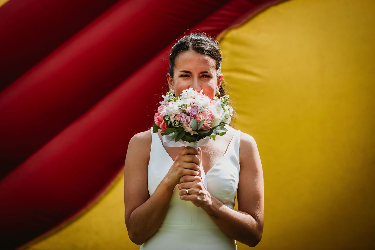 Bride in white dress holding pink and white wedding bouquet in front of red and yellow background.