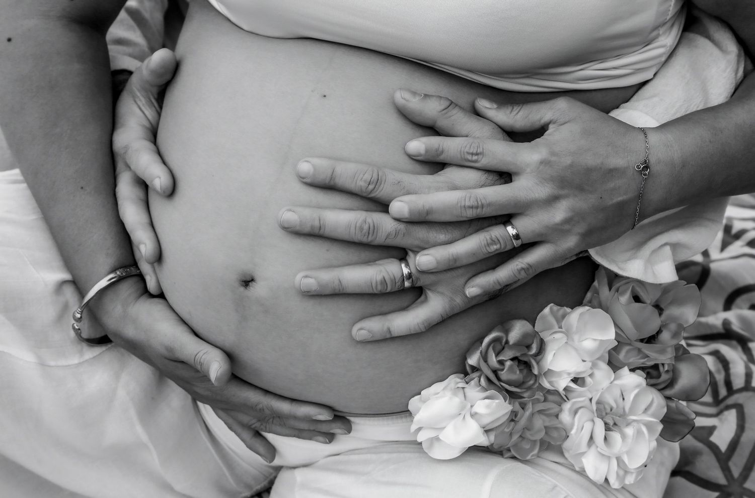 Black and white photo of couple's hands cradling pregnant belly with flowers, maternity photography.