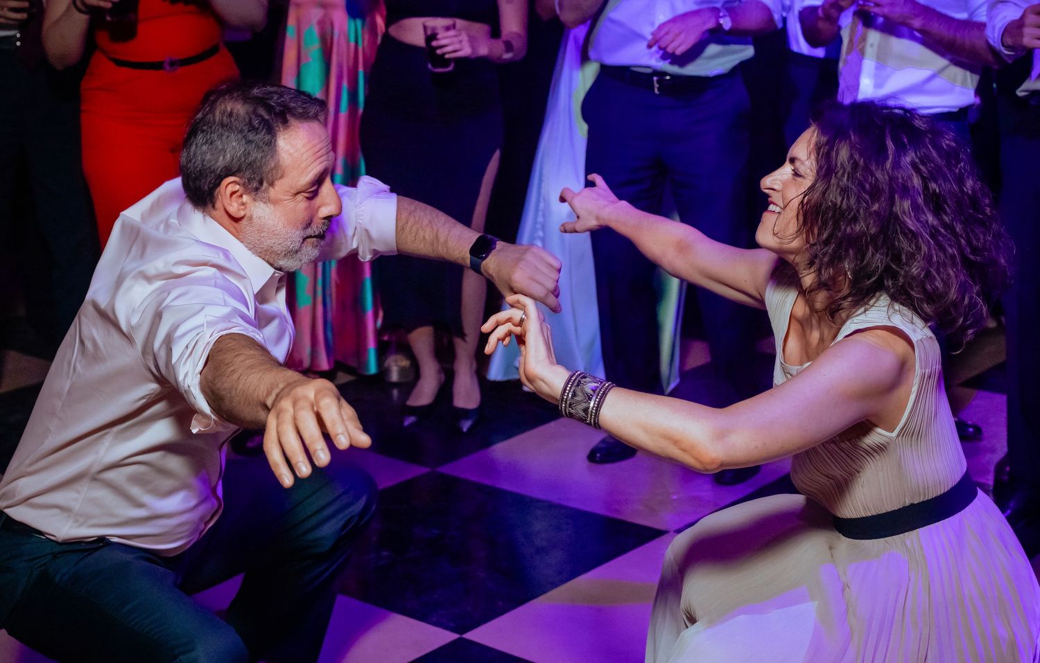 Man and woman engage in energetic low dance move together on checkered wedding reception dance floor.