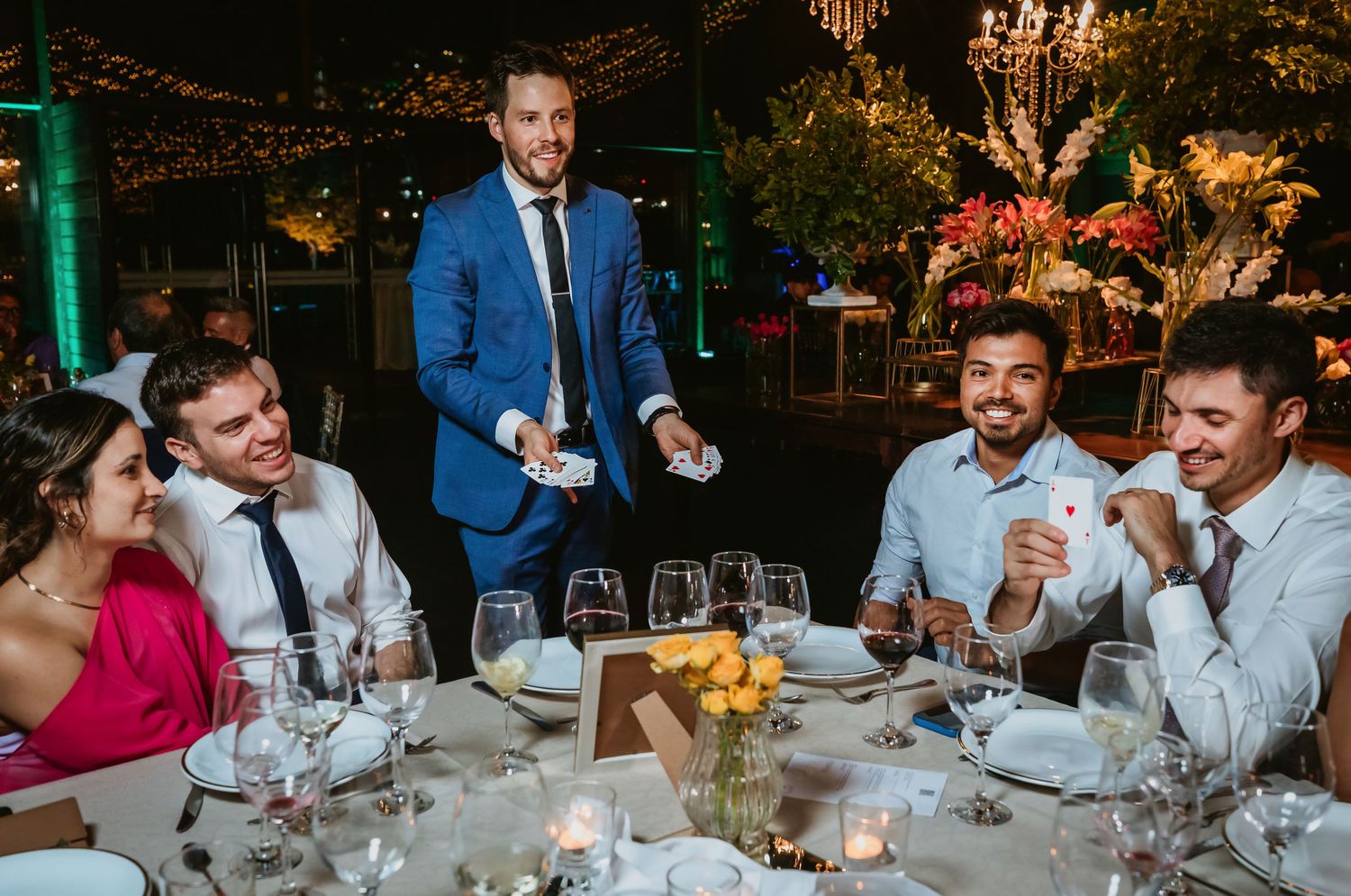 Man in blue suit performing magic tricks for guests at an elegant wedding reception dinner table.