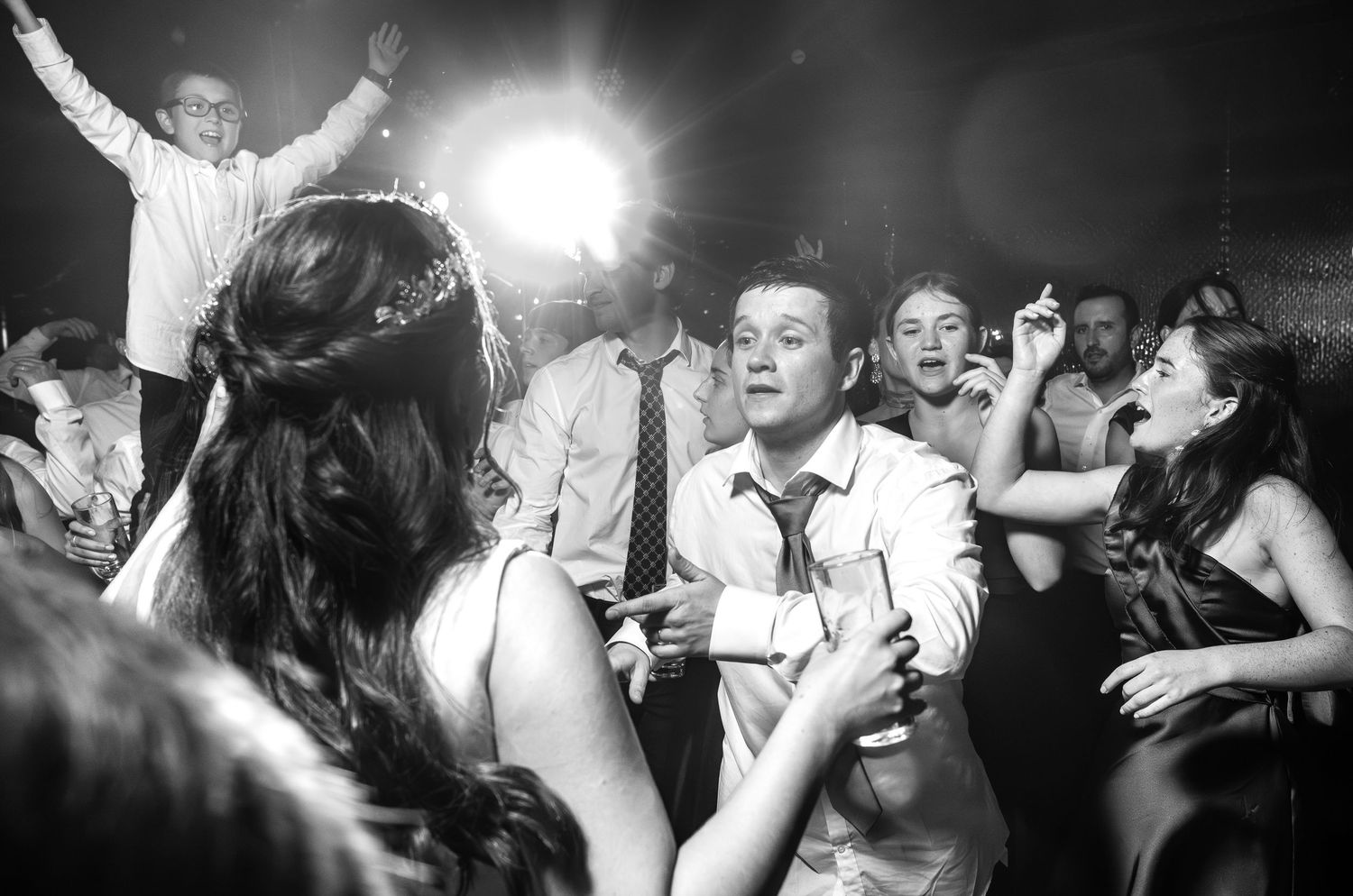 Black and white photo of lively wedding reception dancing with bride and groom celebrating with guests.