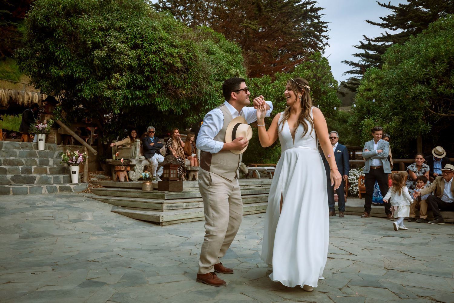 Bride and groom laughing and drinking together during their outdoor wedding celebration on a stone dance floor.
