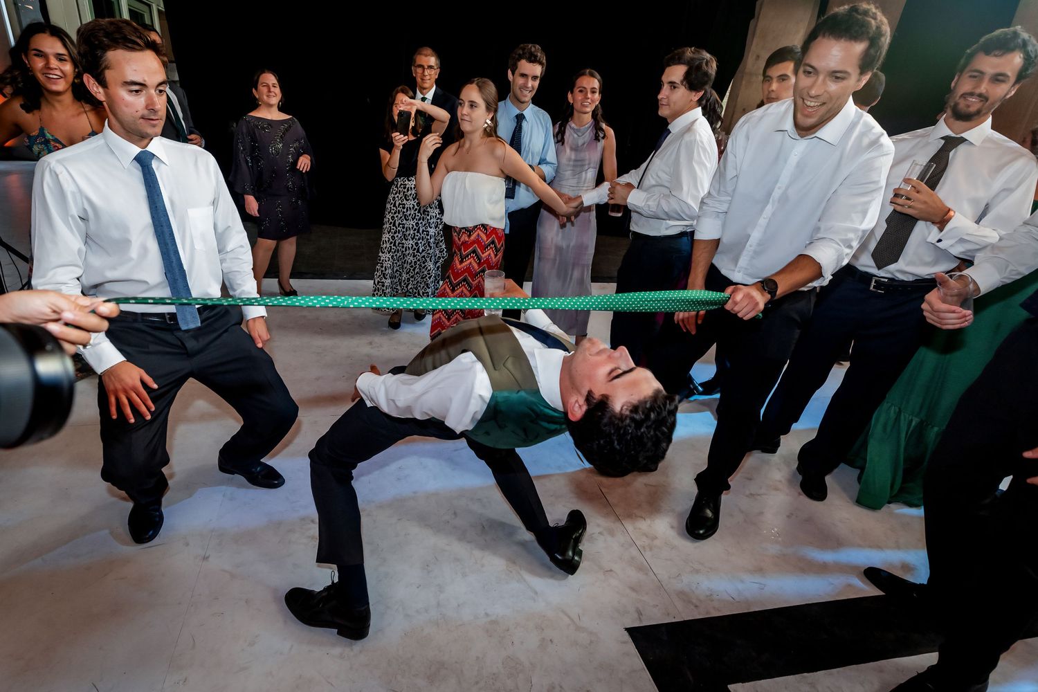 Wedding guests play limbo under a green band on the dance floor.