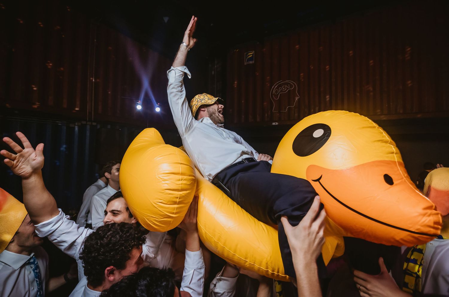 Man riding giant inflatable rubber duck crowd surfing at a lively party event.