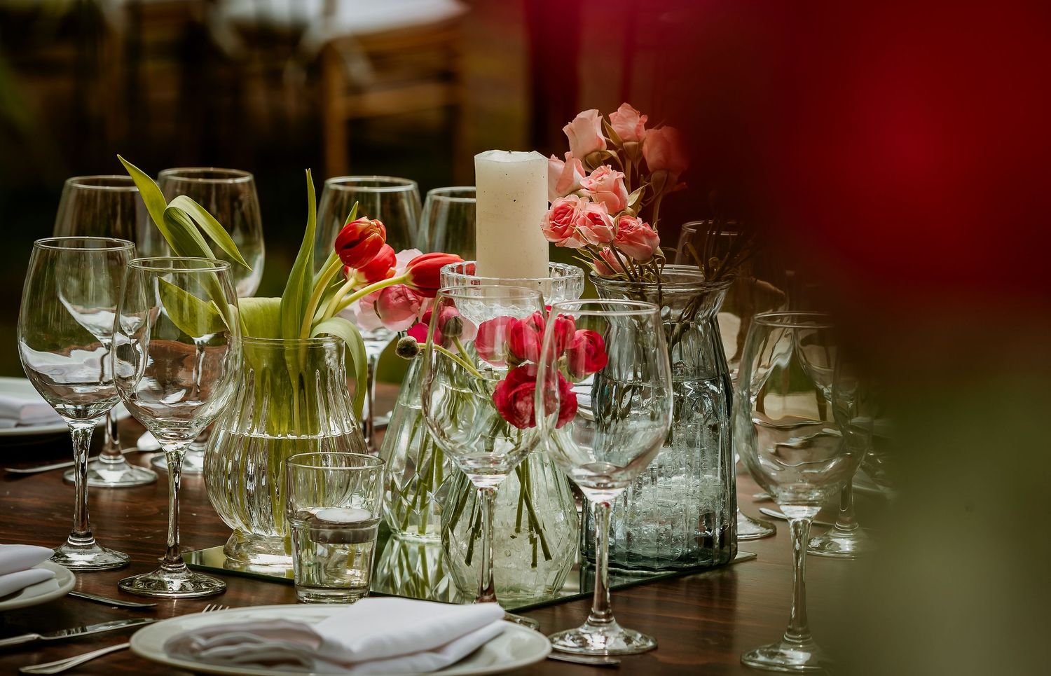 Elegant table setting with crystal glasses, white candle, and fresh pink tulips in glass vases for a formal event.