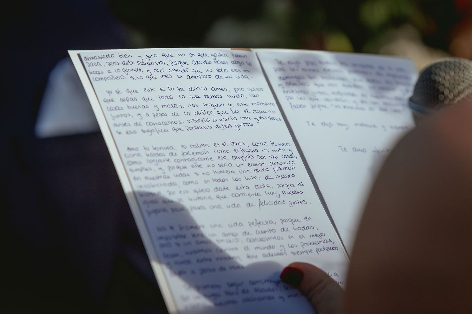 Close-up of handwritten wedding vows on paper held during outdoor wedding ceremony.