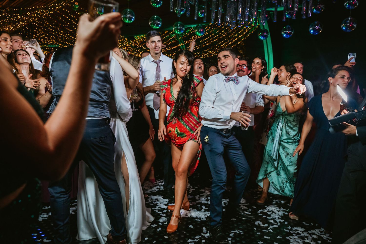 Guests dancing energetically on wedding reception dance floor with confetti falling around them.