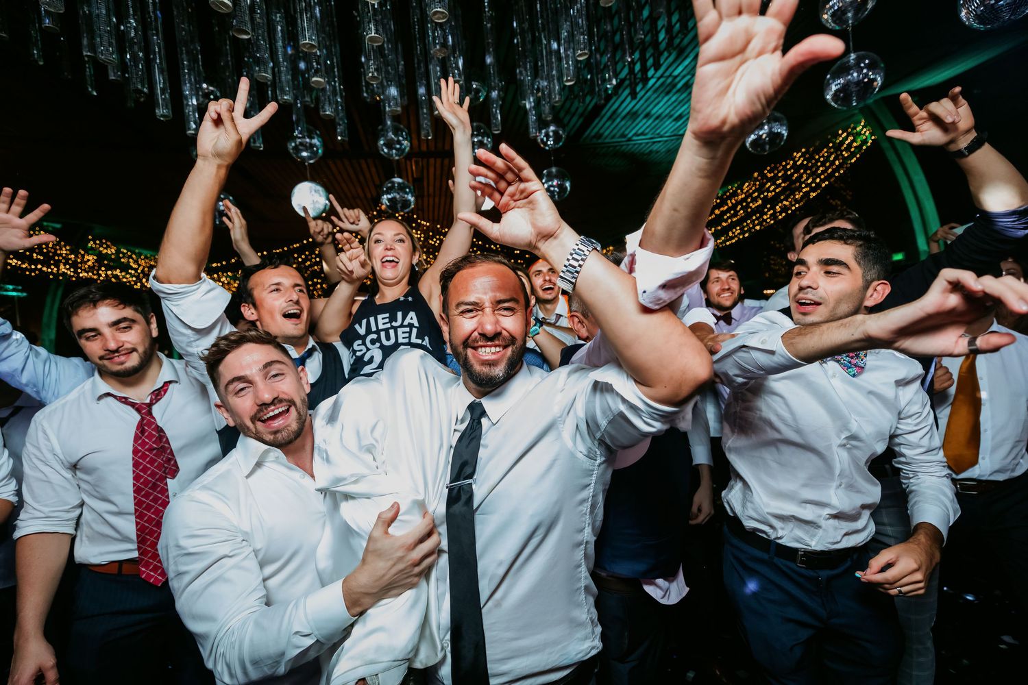 Groom and male guests celebrate enthusiastically on a festive wedding dance floor.