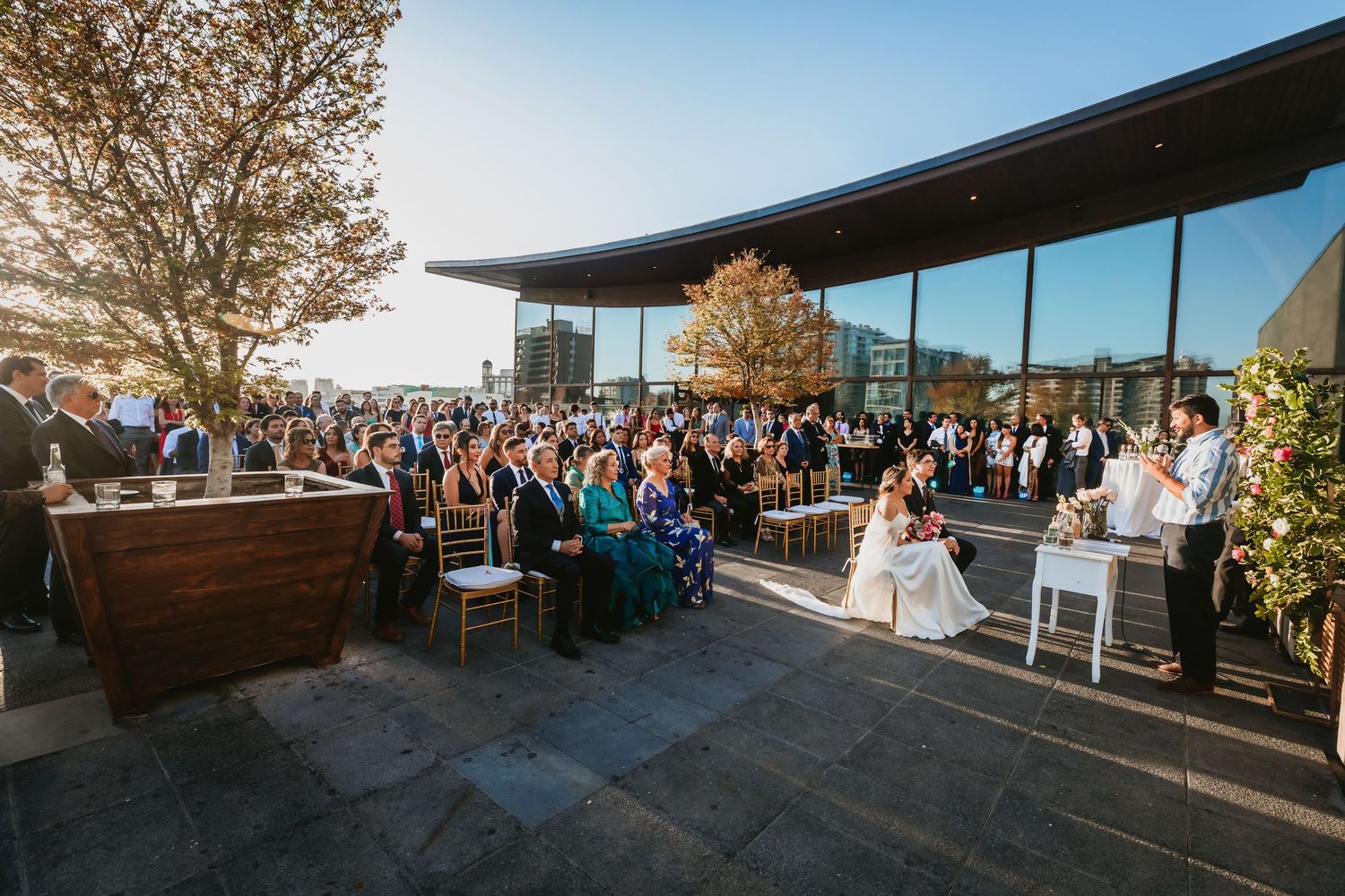 Large outdoor rooftop wedding ceremony with guests seated facing couple at altar.