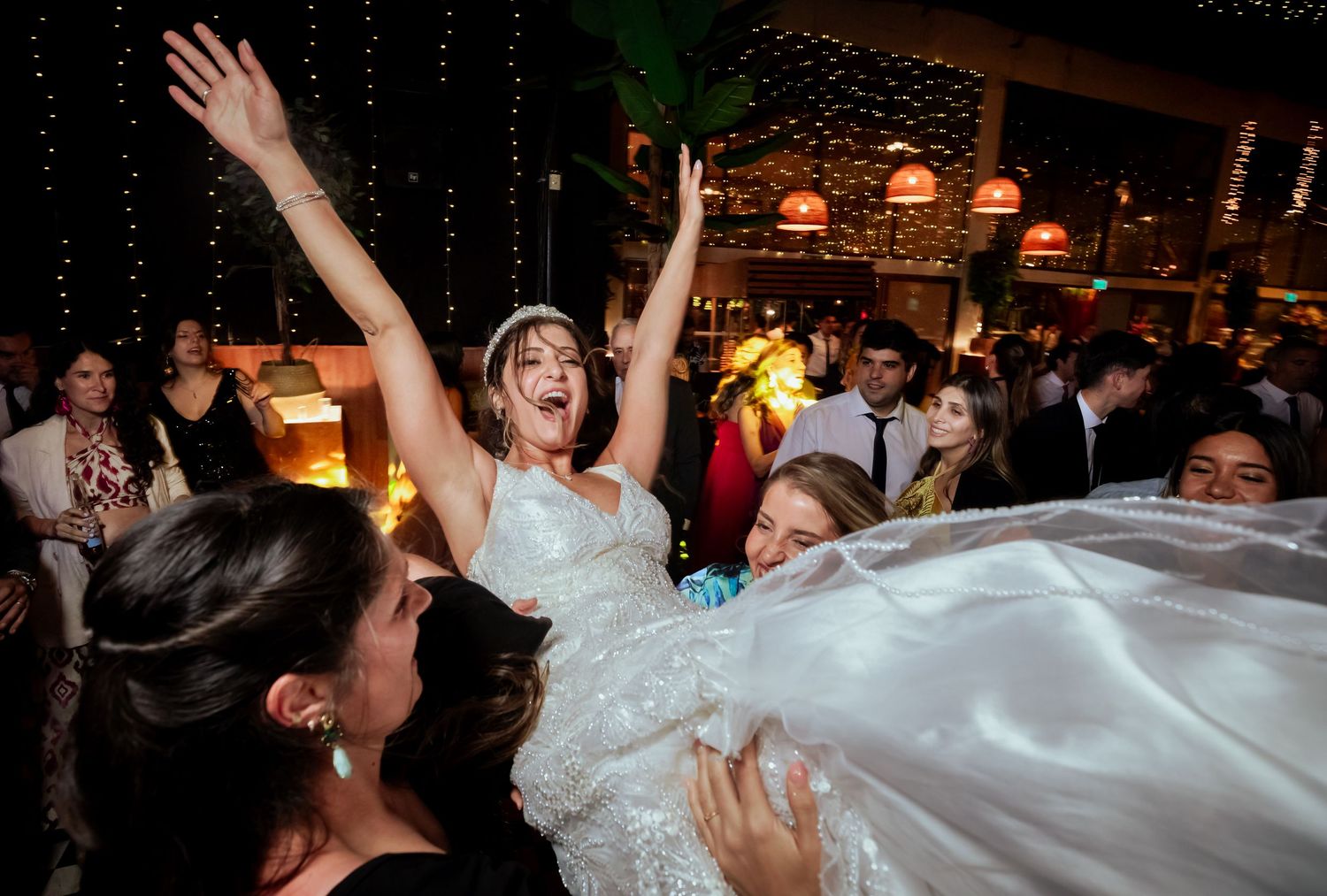 Bride is lifted joyfully by guests during an energetic wedding reception celebration.
