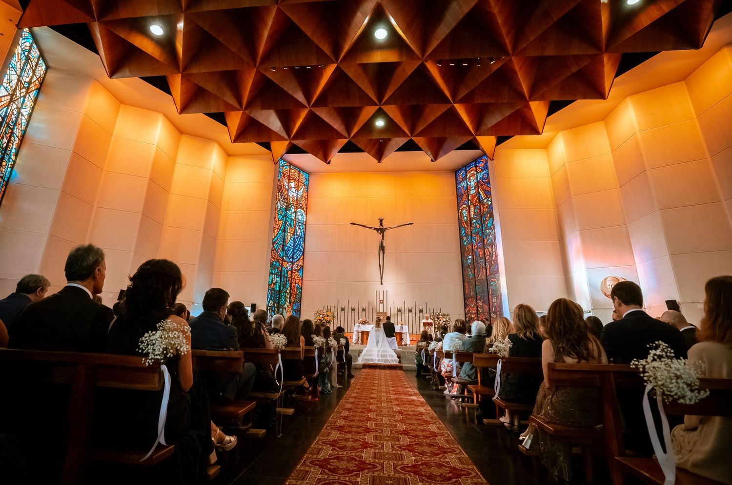 Wide angle view of elegant church wedding ceremony with guests seated in pews and couple at the altar.