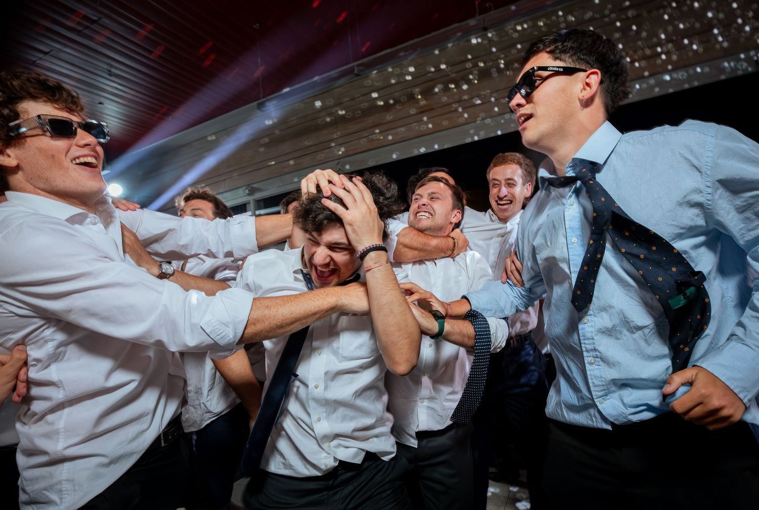 Groomsmen in white shirts celebrate and roughhouse together at lively wedding reception.