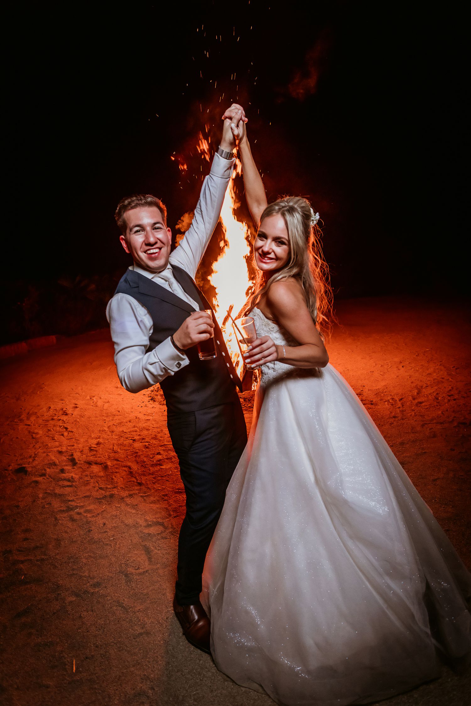 Smiling bride and groom hold sparkler together on beach at night wedding.