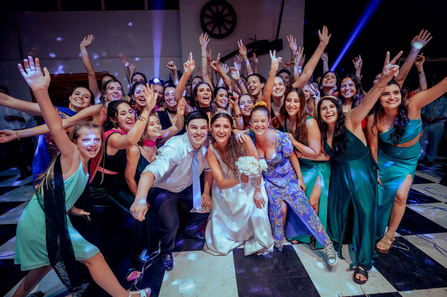 Bride and groom pose with large group of wedding guests on dance floor.