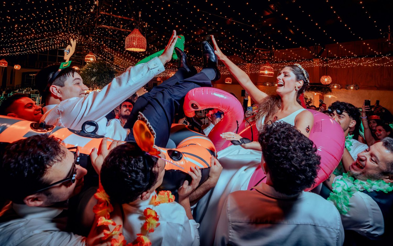 Groom lifted by wedding guests during lively reception party celebration.