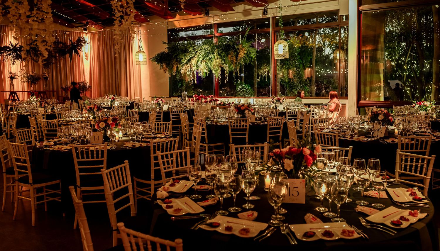 Warmly lit wedding banquet hall with round tables, chiavari chairs, and floral decor.