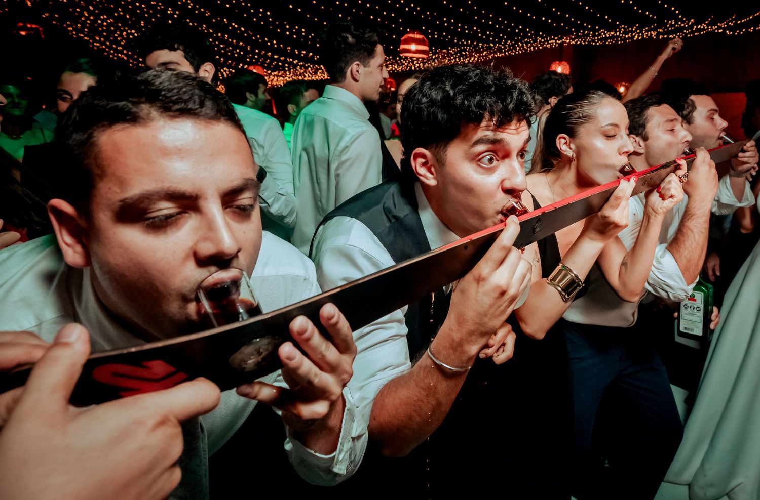 Wedding guests take shots from red tubes at lively wedding reception party celebration.