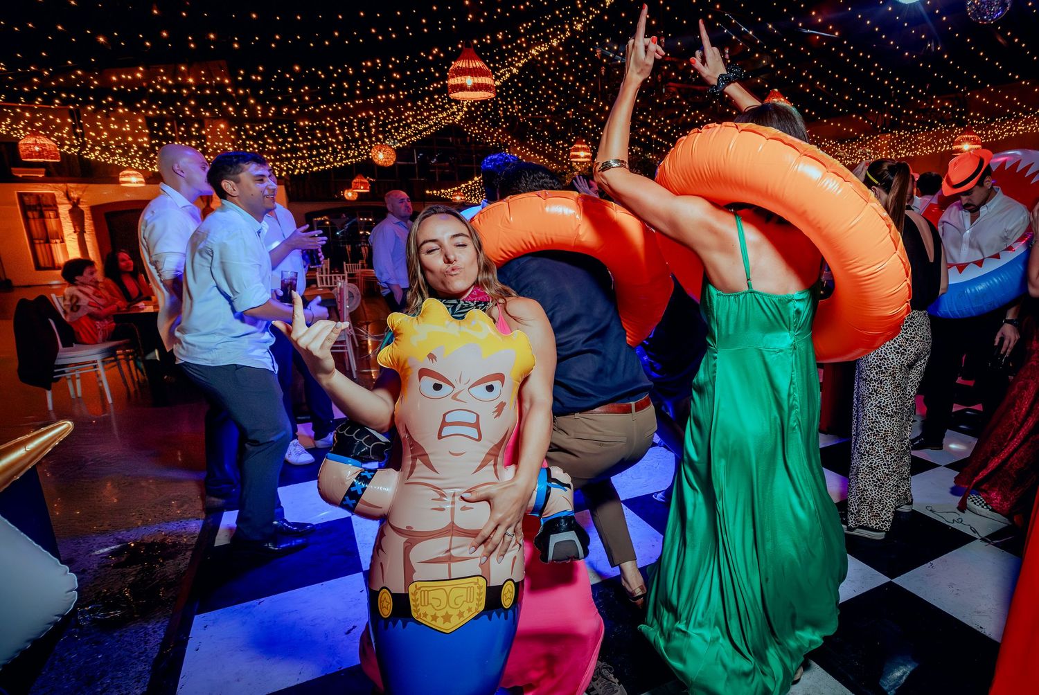 Woman posing with superhero inflatable toy and orange pool ring at a fun wedding reception.
