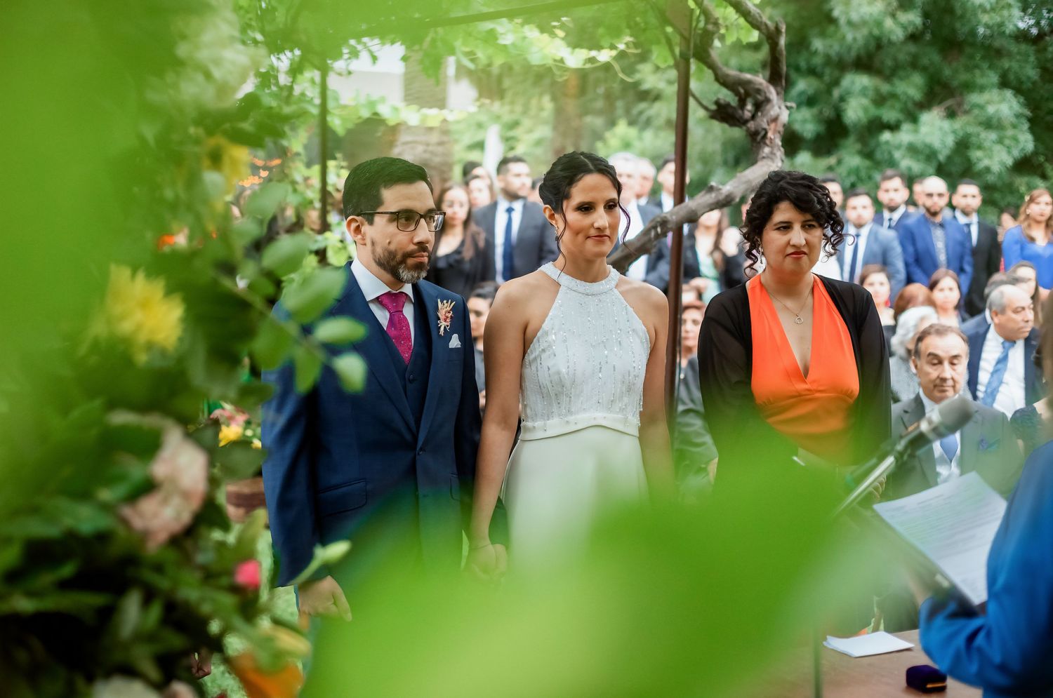 Bride and groom share intimate ceremony moment framed by lush green foliage at outdoor garden wedding.
