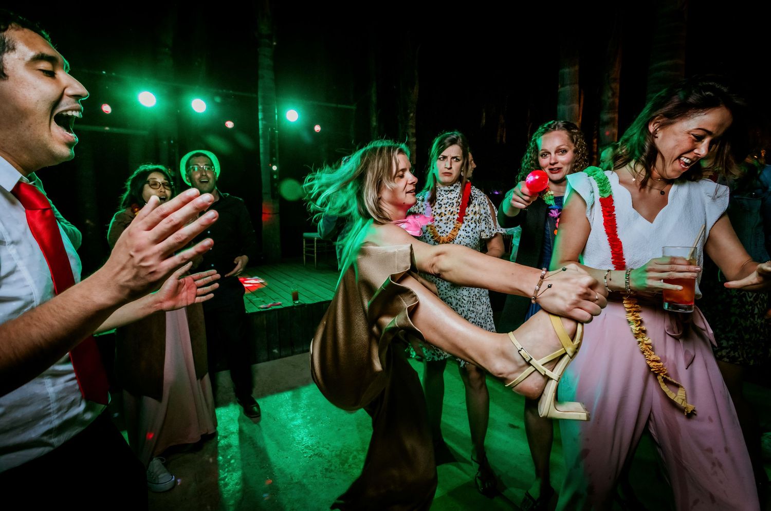 Wedding guests dancing energetically under green lights at a lively outdoor reception.
