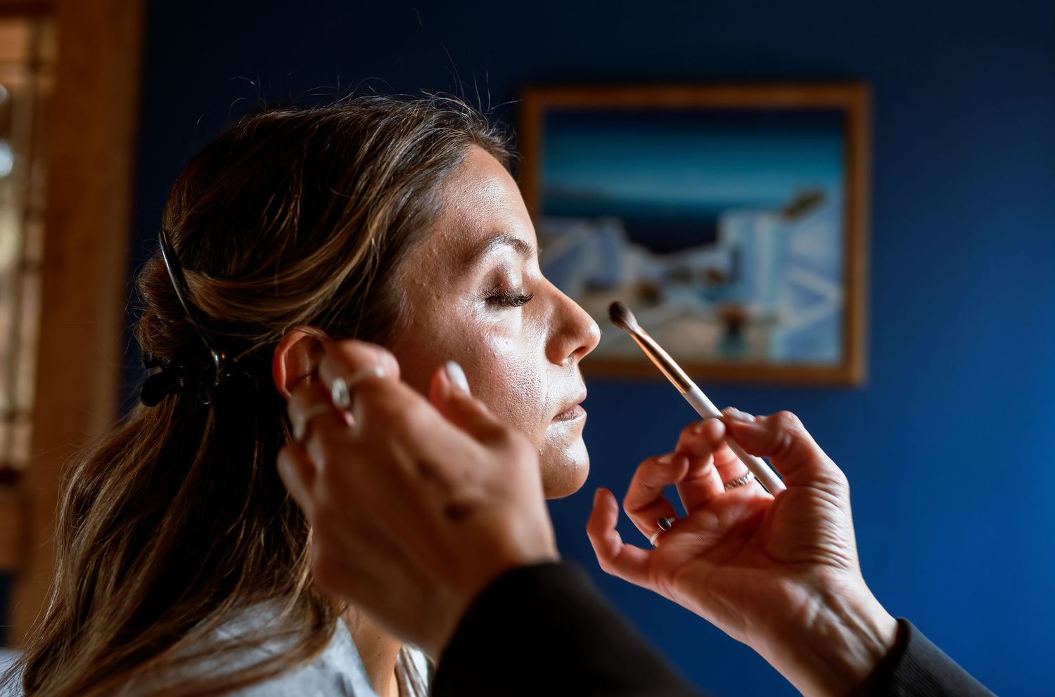 Makeup artist applying foundation to brides face with brush before wedding.
