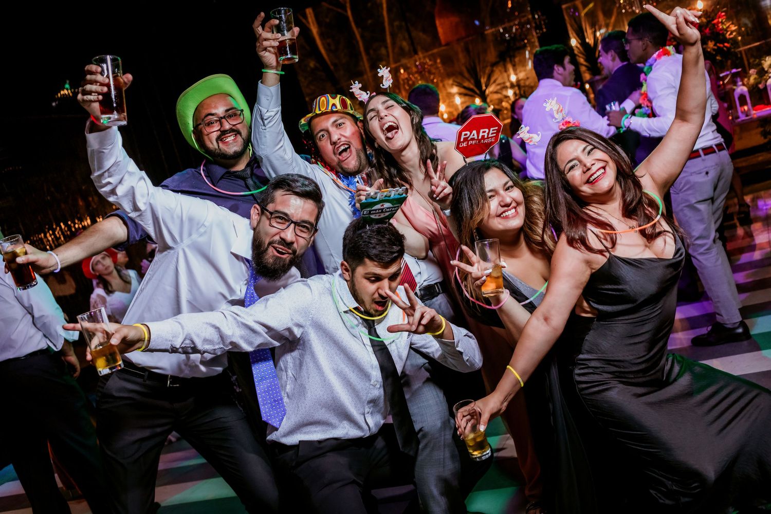 Group of energetic wedding guests dance and celebrate together on a colorful dance floor at a night reception.