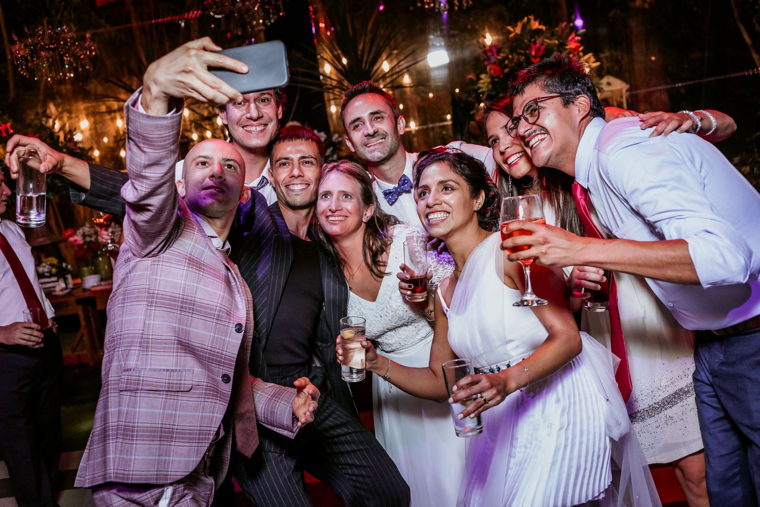Wedding guests take a fun group selfie while celebrating at a reception party with drinks.