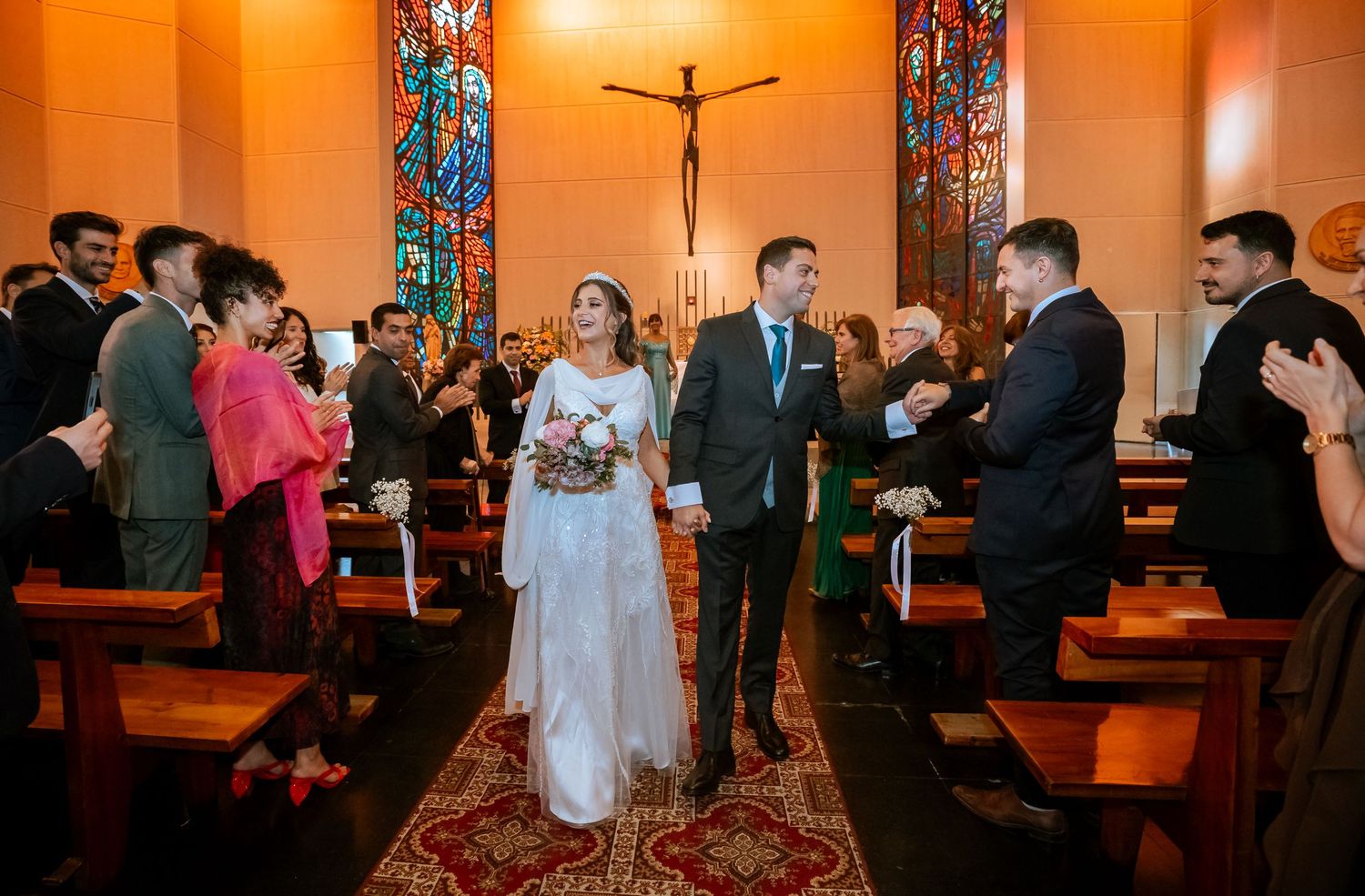 Newlyweds walk down the aisle together as guests celebrate their Catholic church wedding ceremony.