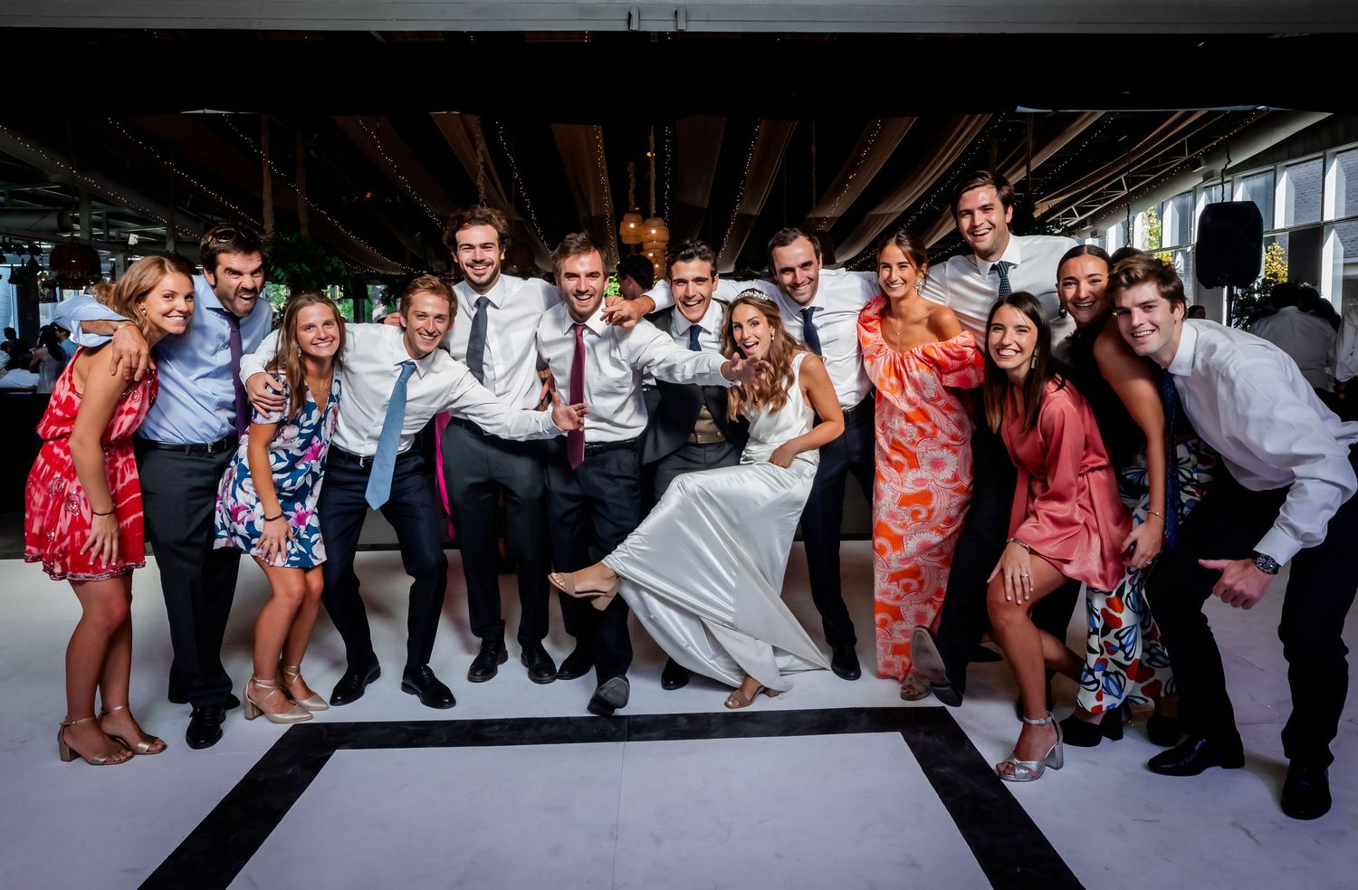 Wedding party and guests laugh and pose together on the dance floor.