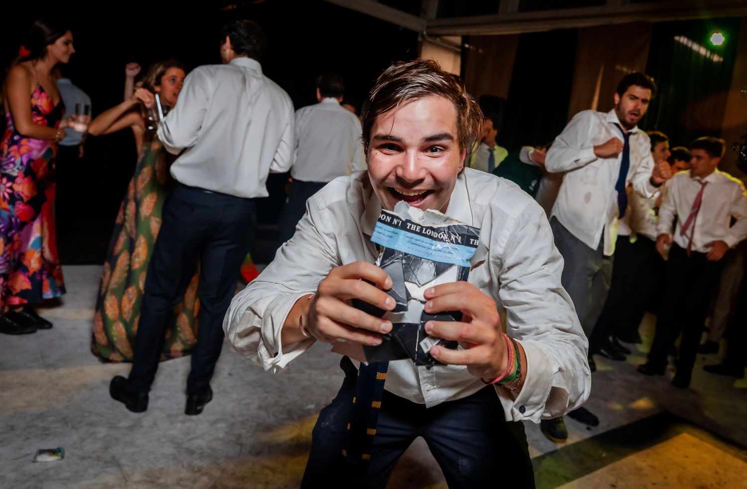 Happy man smiles while holding a camera at a fun wedding reception dance floor.