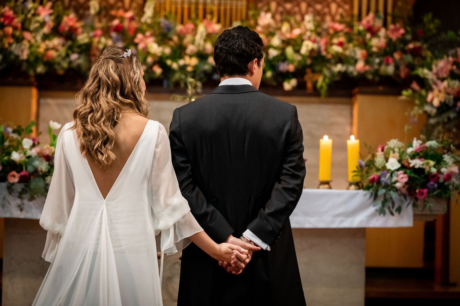 Bride and groom holding hands facing floral altar during romantic church wedding ceremony.