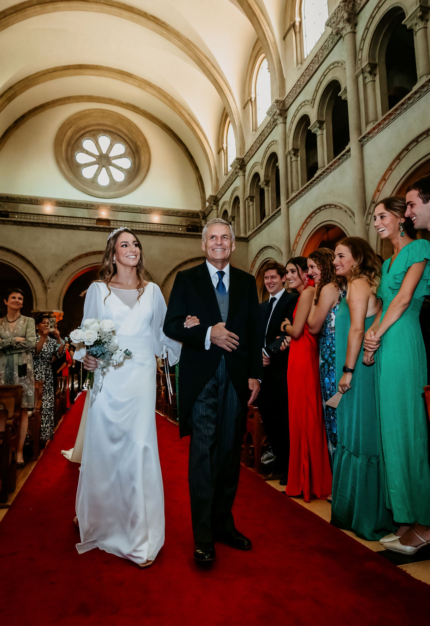 Bride and father walking red carpet aisle in magnificent church with rose window and stone arches.