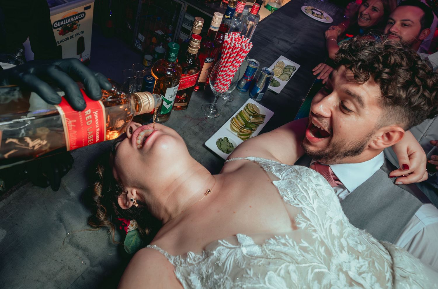 Bride leaning back receiving a bottle drink pour at a fun wedding reception.