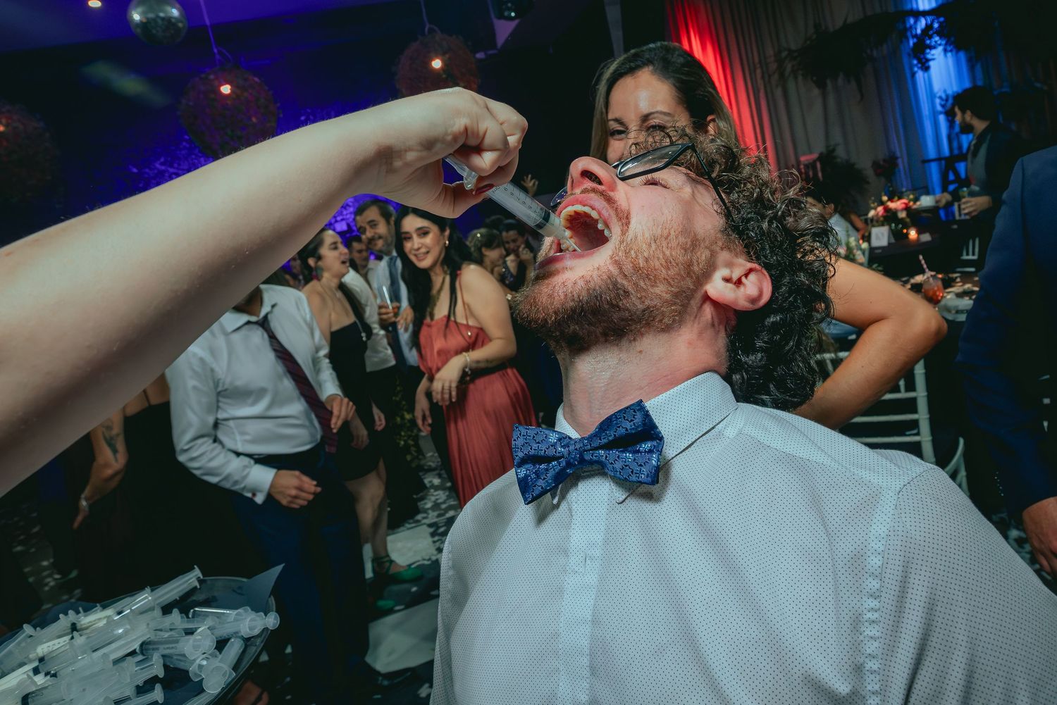 Curly-haired man in blue bow tie catching drink at festive wedding reception party.