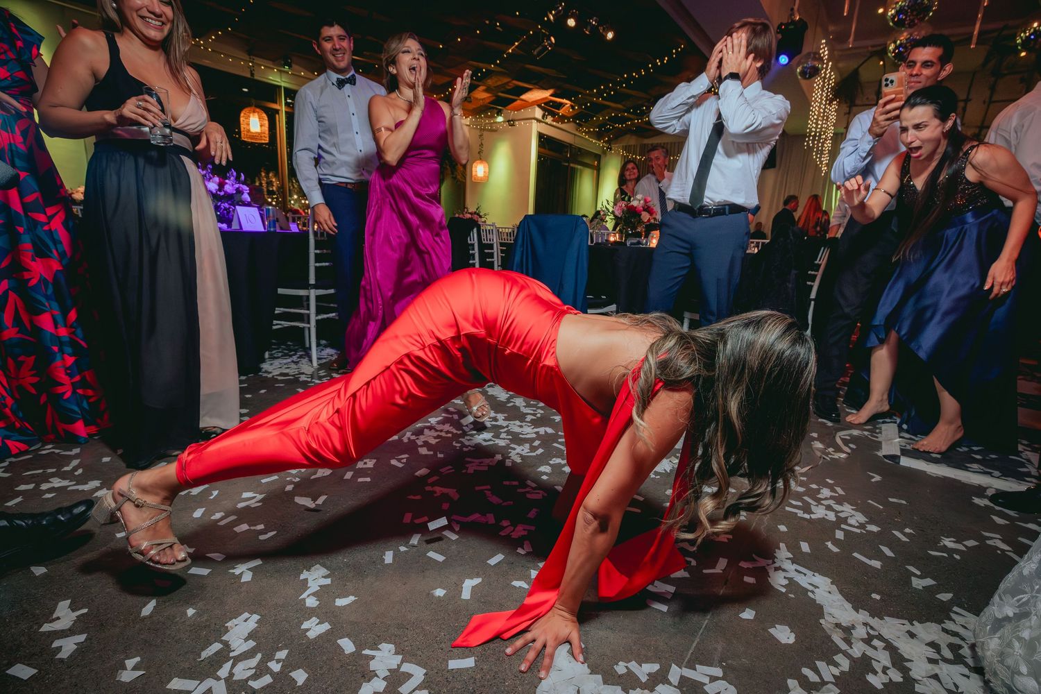 Woman in red outfit dancing energetically on confetti-covered wedding reception floor.
