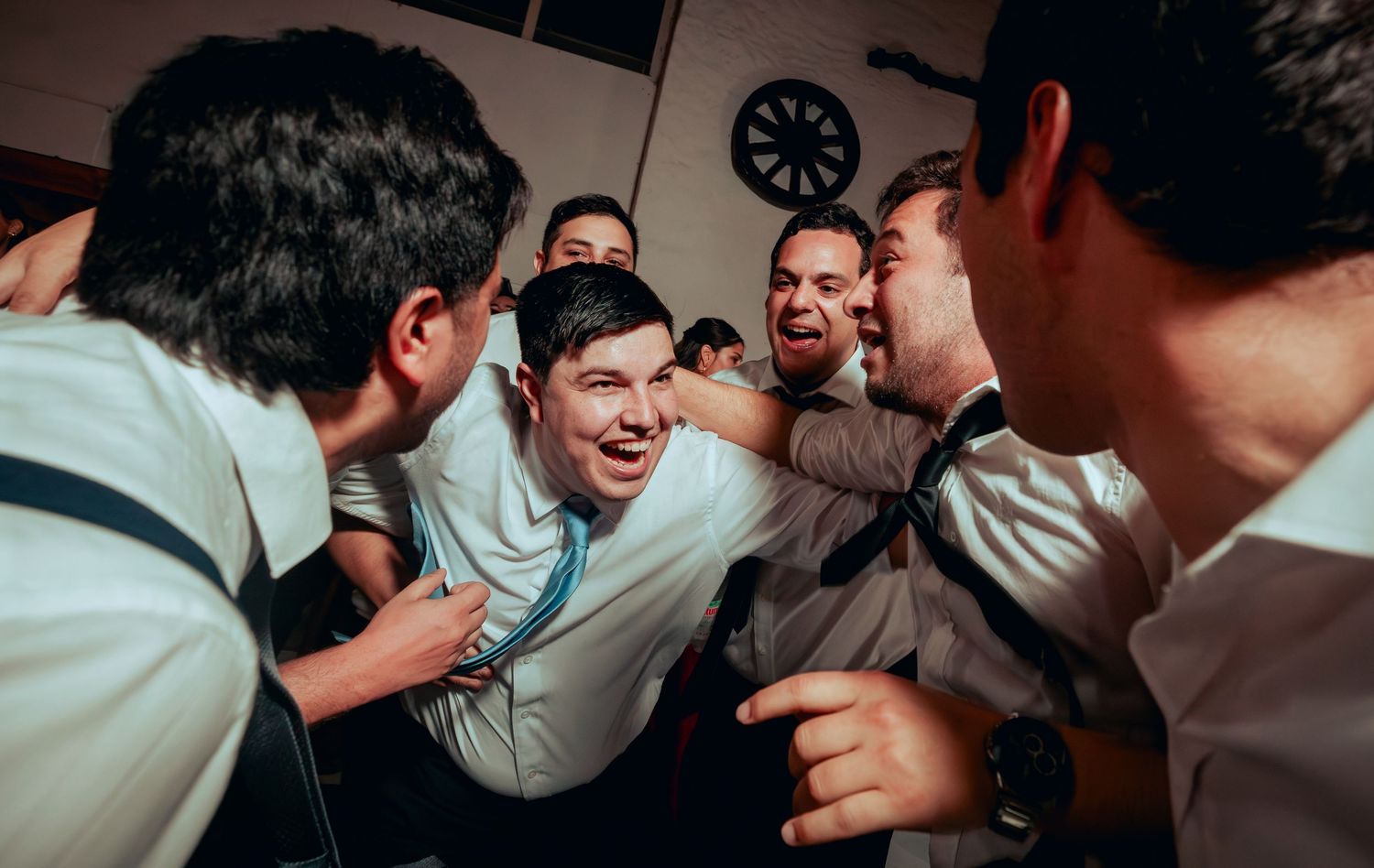 Groom surrounded by groomsmen in tight celebratory huddle at fun wedding reception gathering.