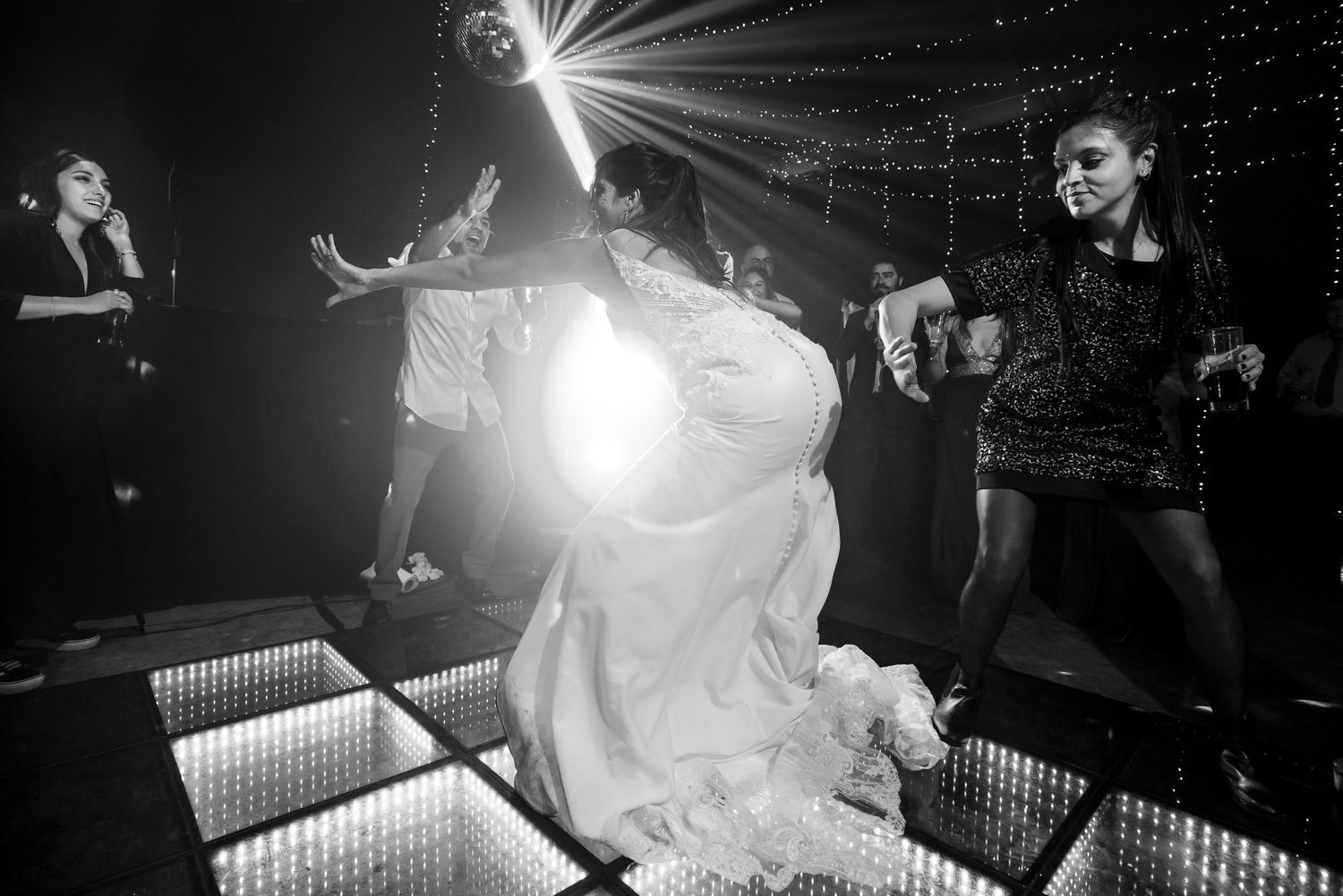 Bride dancing energetically on illuminated dance floor in black and white wedding reception photo.