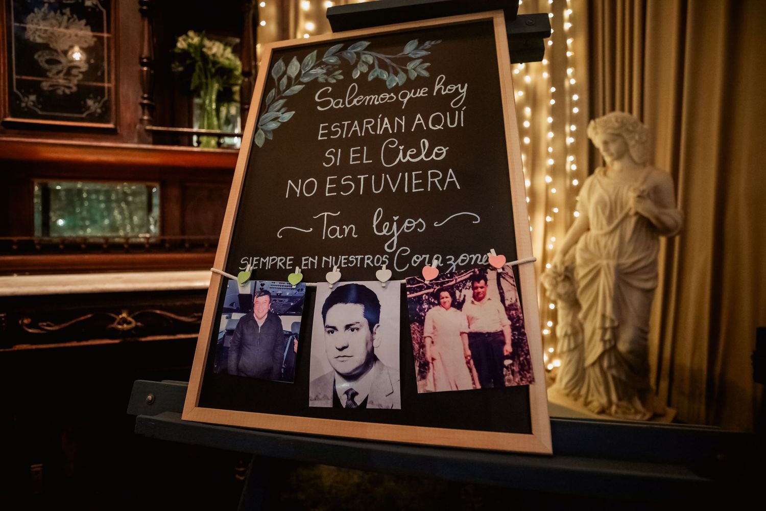 Wedding memorial chalkboard sign honoring absent loved ones, decorated with vintage photos and fairy lights.