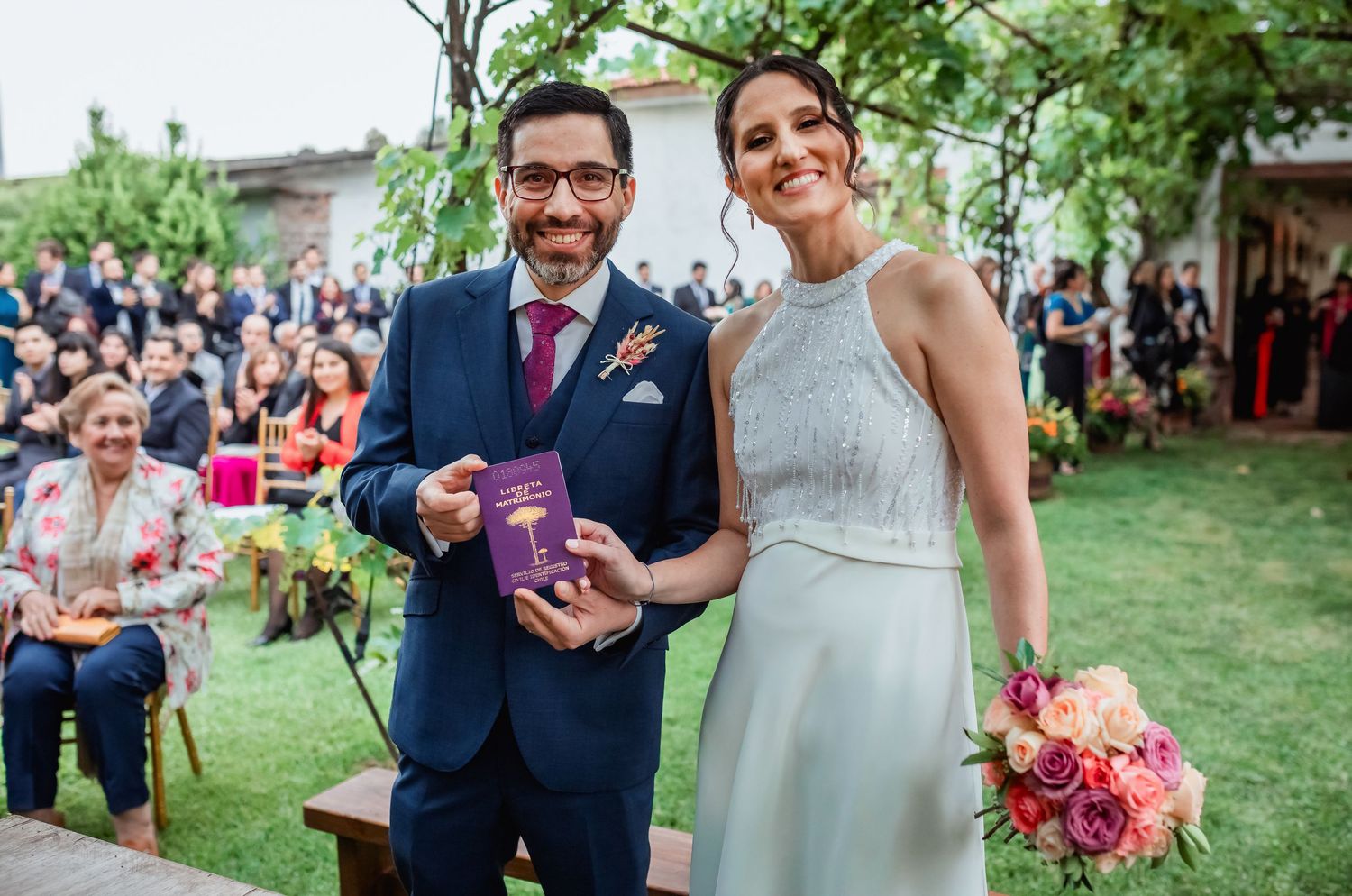 Newlyweds smile holding wedding certificate at outdoor garden wedding ceremony.